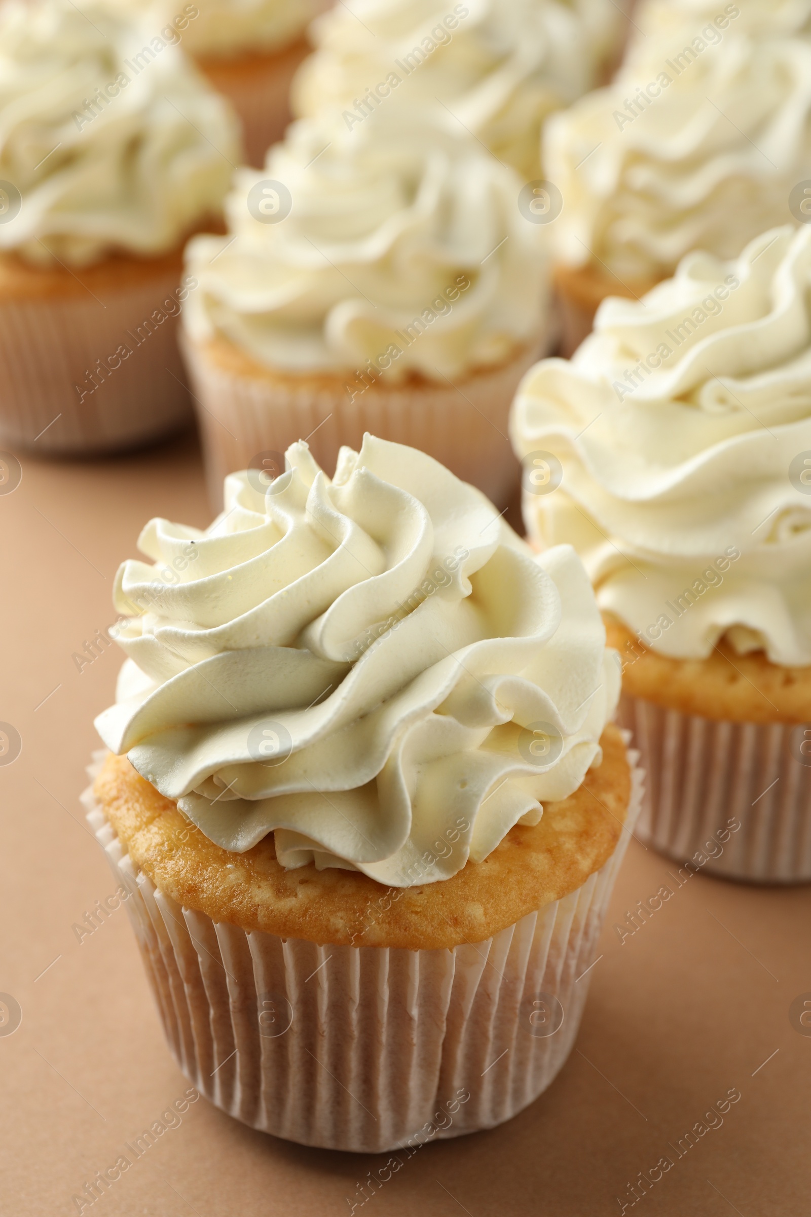 Photo of Tasty vanilla cupcakes with cream on beige table, closeup