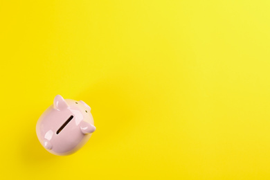 Photo of Pink piggy bank on yellow background, top view. Space for text