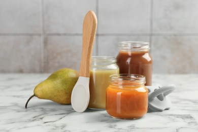 Tasty baby food in jars, pear and spoon on white marble table