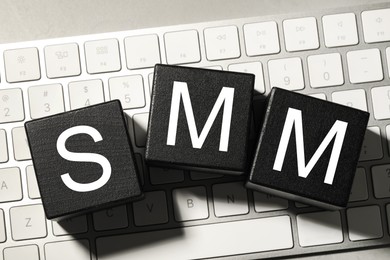Photo of Black cubes with letters SMM on computer keyboard, flat lay