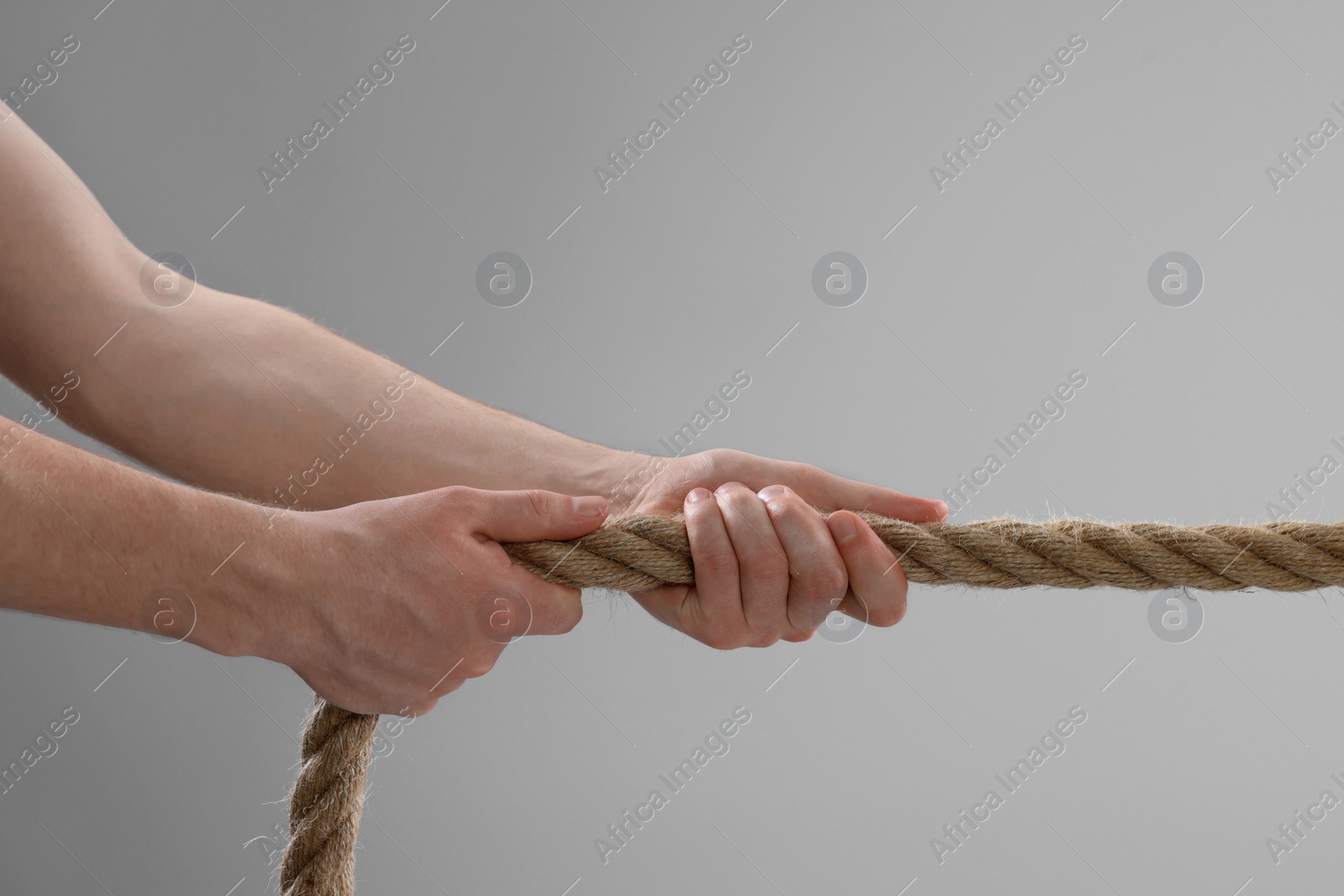 Photo of Dispute concept. Man pulling rope on light grey background, closeup