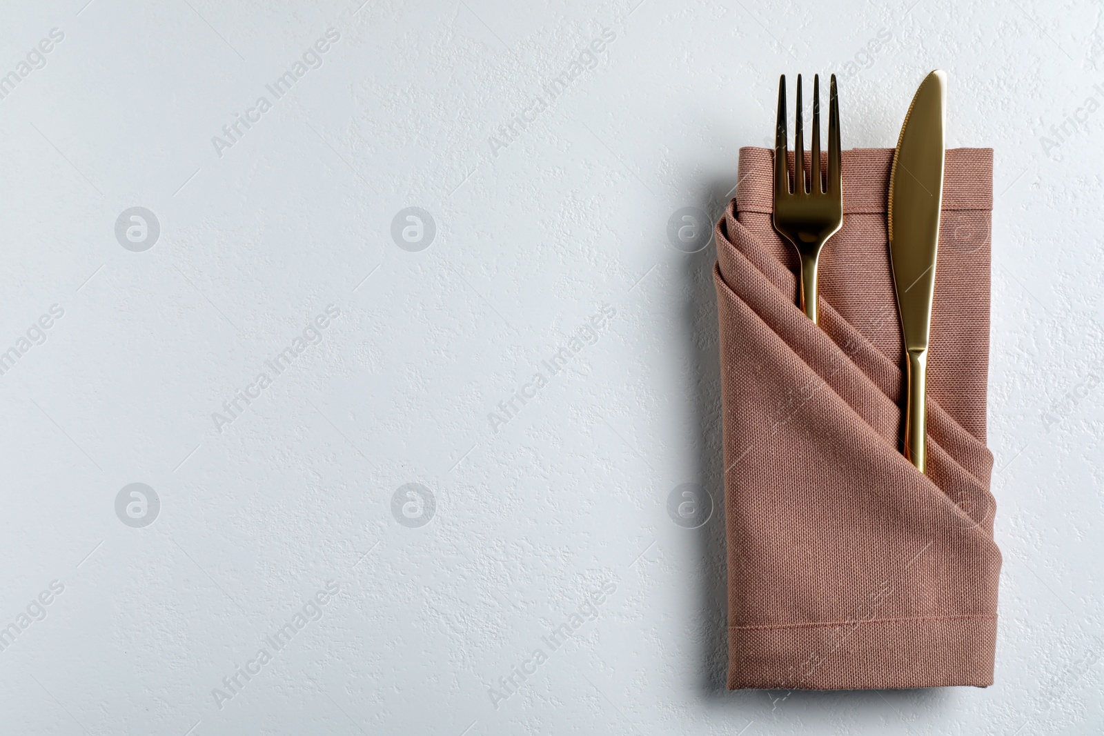 Photo of Golden fork and knife with napkin on white table, top view. Space for text