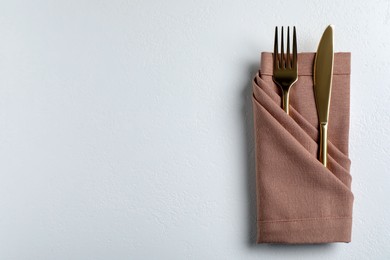 Photo of Golden fork and knife with napkin on white table, top view. Space for text