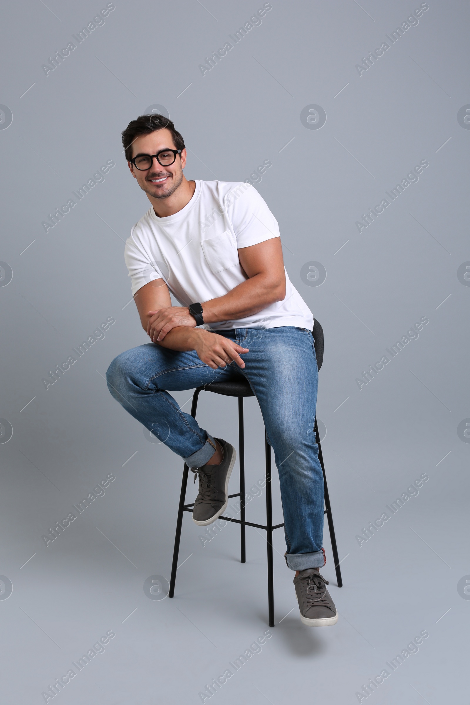 Photo of Handsome young man sitting on stool against grey background