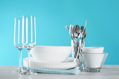 Set of clean dishes, glasses and cutlery on table against color background