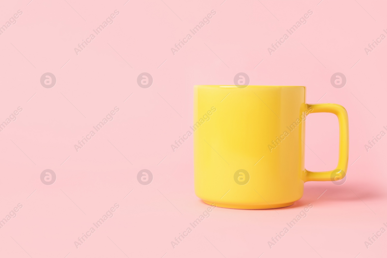 Photo of One yellow ceramic mug on pink background, space for text