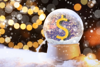 Image of Snow globe with dollar sign and blurred Christmas lights on background. Space for text