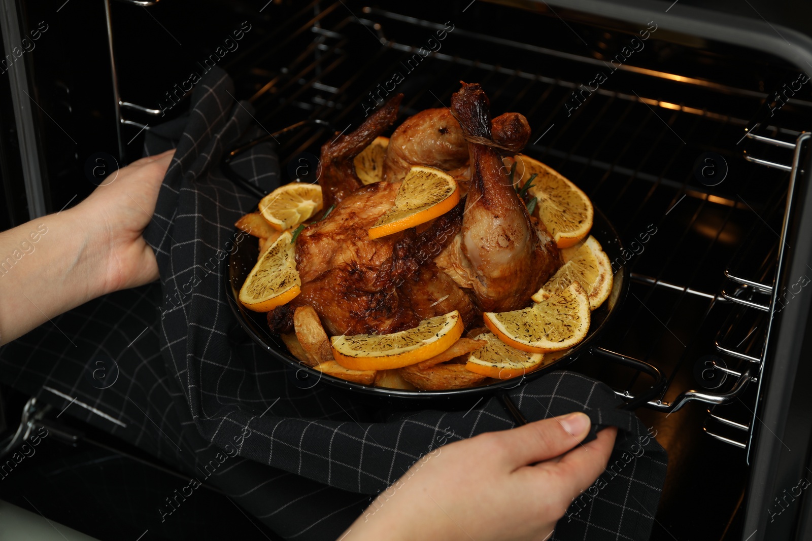 Photo of Woman taking baked chicken with orange slices out of oven, closeup