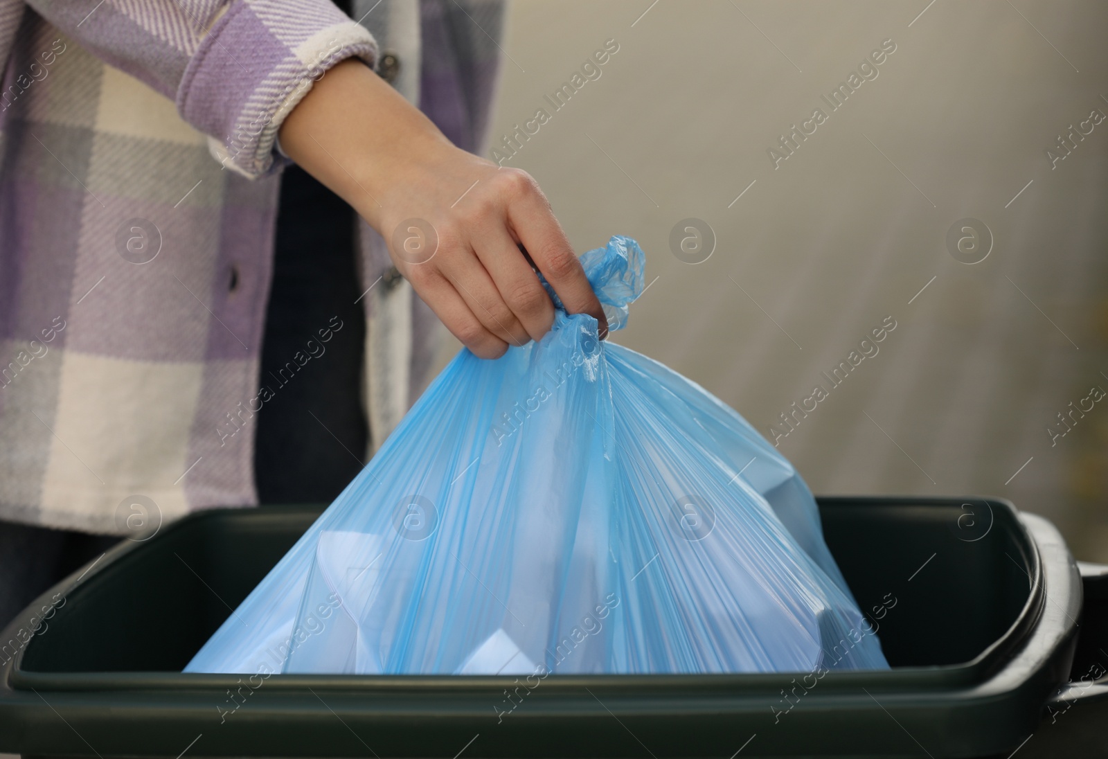 Photo of Woman putting garbage bag into recycling bin outdoors, closeup