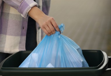 Woman putting garbage bag into recycling bin outdoors, closeup