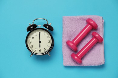 Photo of Alarm clock, towel and dumbbells on light blue background, flat lay. Morning exercise