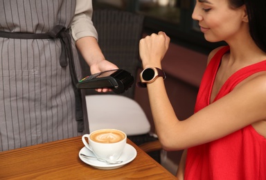 Woman making payment with smart watch in cafe, closeup