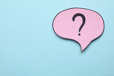 Paper speech bubble with question mark on light blue background, top view. Space for text