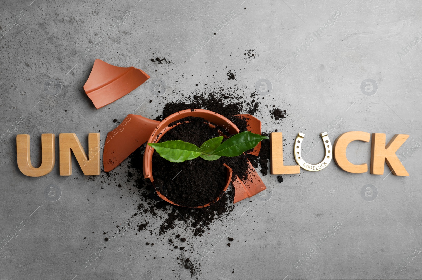 Photo of Word UNLUCK made of wooden letters and plant in broken pot on grey stone table, flat lay