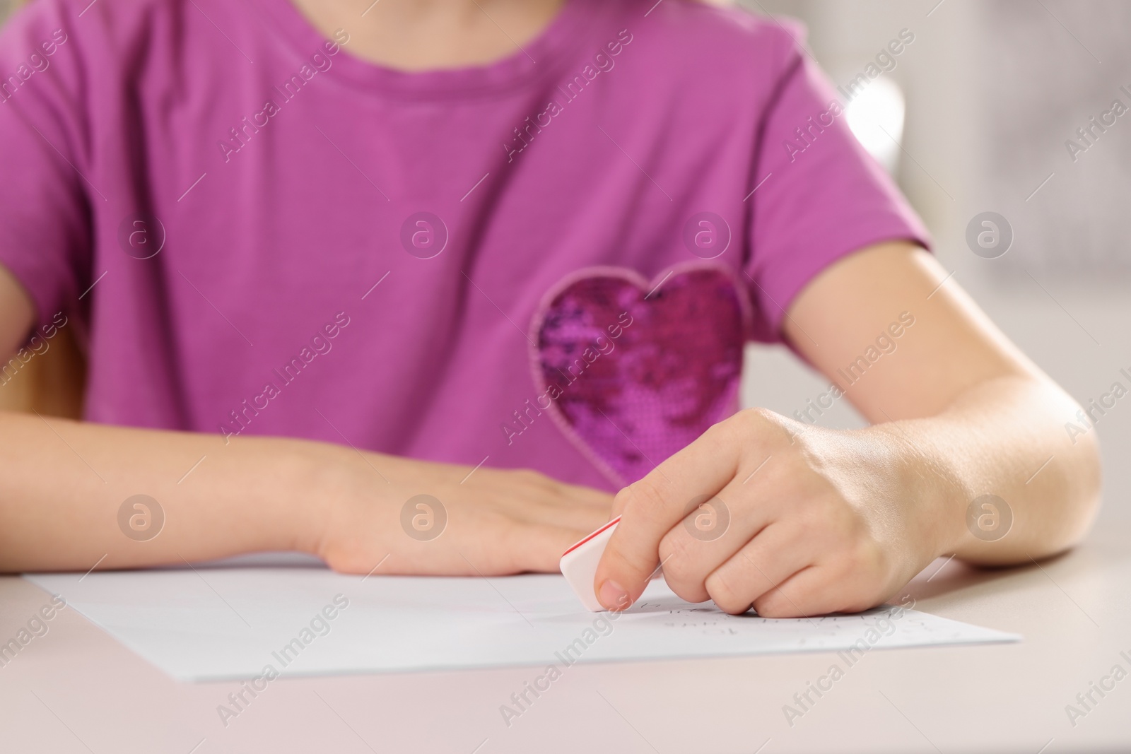 Photo of Girl erasing mistake in her homework at white desk, closeup