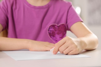 Girl erasing mistake in her homework at white desk, closeup