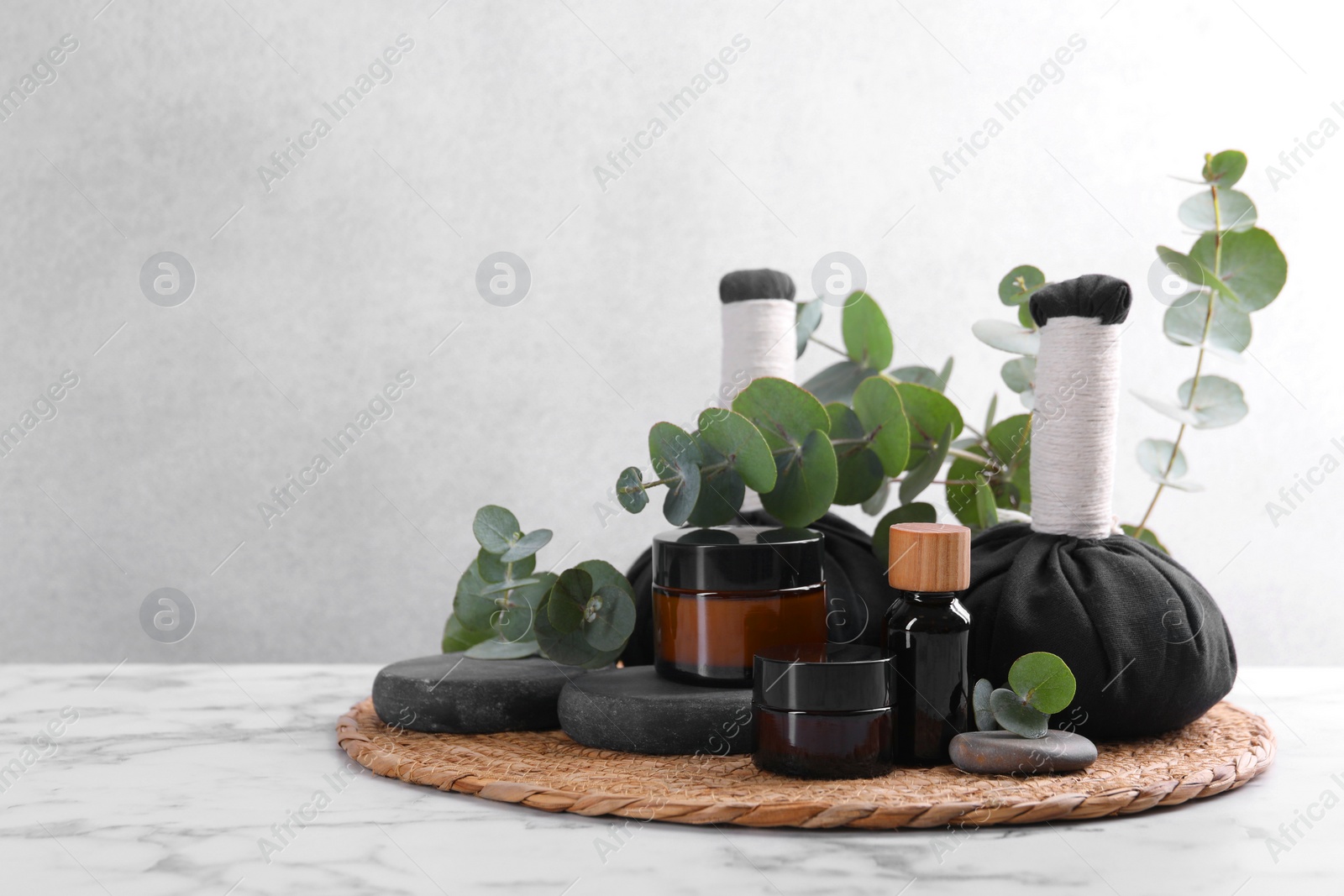 Photo of Spa composition with cosmetic products, herbal massage bags, stones and eucalyptus branches on white marble table, space for text