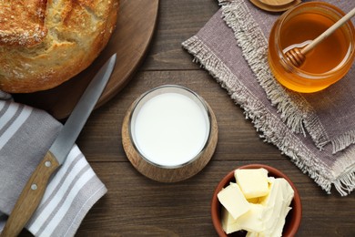 Glass with fresh milk, honey, butter and bread on wooden table, flat lay