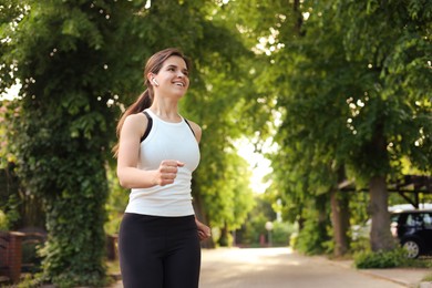 Young woman with wireless earphones jogging outdoors in morning