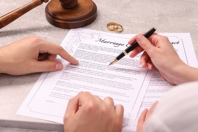 Man and woman signing marriage contract at light grey table, closeup