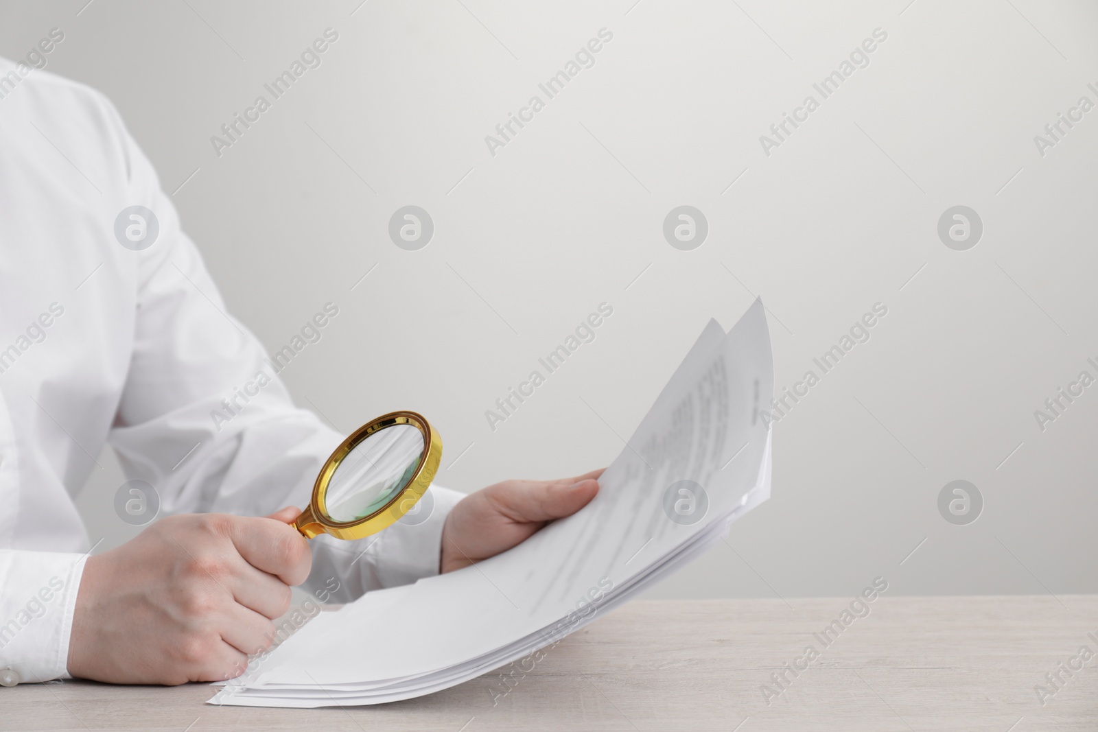 Photo of Man looking at document through magnifier at white wooden table, closeup. Searching concept