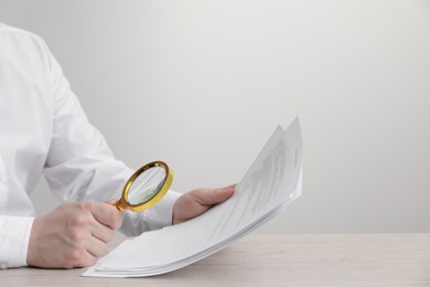 Man looking at document through magnifier at white wooden table, closeup. Searching concept