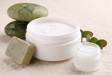 Photo of Composition with body care cream in open jars and soap bar on light textured table, closeup