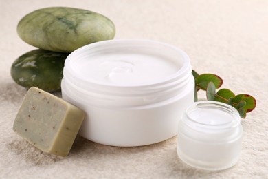 Composition with body care cream in open jars and soap bar on light textured table, closeup