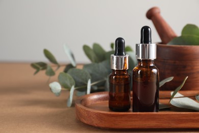 Photo of Aromatherapy. Bottles of essential oil and eucalyptus leaves on brown table, closeup. Space for text