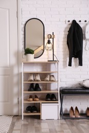 Photo of Shelving unit with shoes and different accessories near white brick wall in hall. Storage idea
