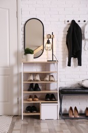 Shelving unit with shoes and different accessories near white brick wall in hall. Storage idea