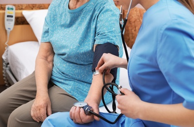 Photo of Nurse measuring senior woman's blood pressure in hospital ward, closeup. Medical assisting