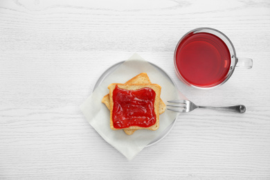 Photo of Tasty toast with jam and raspberry tea on white wooden table, flat lay. Delicious morning meal