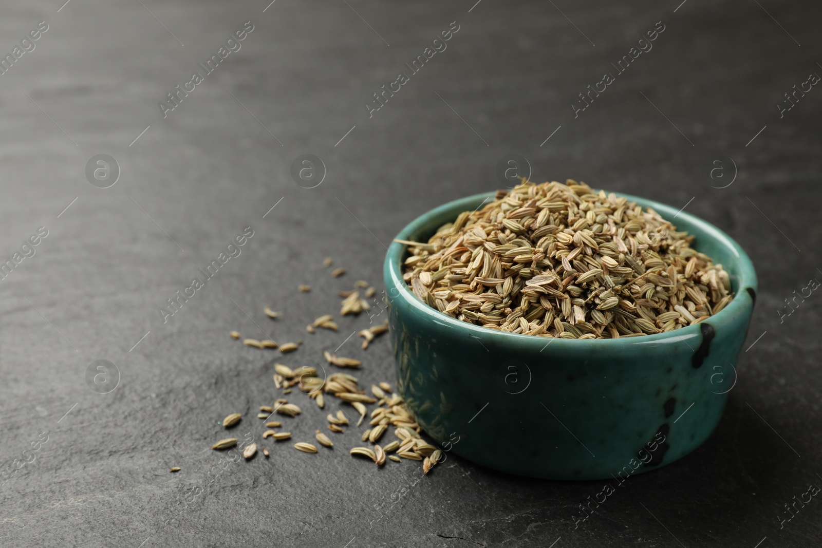 Photo of Fennel seeds in bowl on gray table, closeup. Space for text