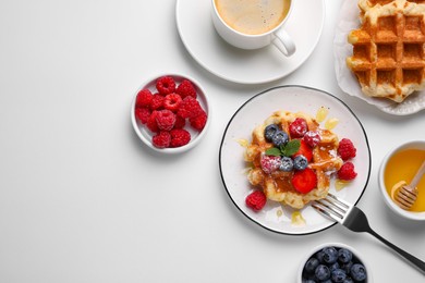 Delicious Belgian waffles with fresh berries and honey served on white table, flat lay. Space for text