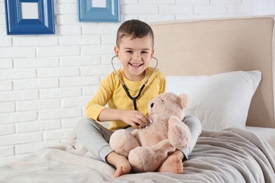 Photo of Cute child playing doctor with stuffed toy at hospital