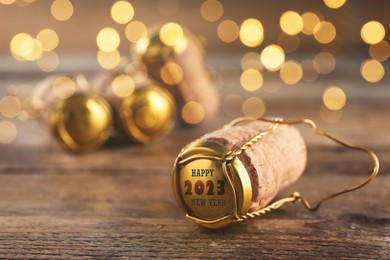 Image of Cork of sparkling wine and muselet cap with engraving Happy 2023 New Year on wooden table, space for text. Bokeh effect