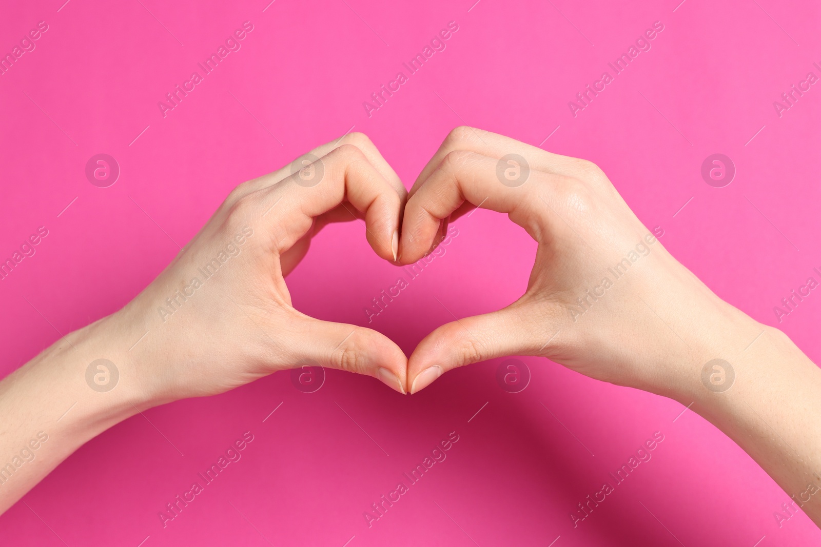 Photo of Woman showing heart gesture with hands on pink background, closeup