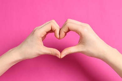 Woman showing heart gesture with hands on pink background, closeup