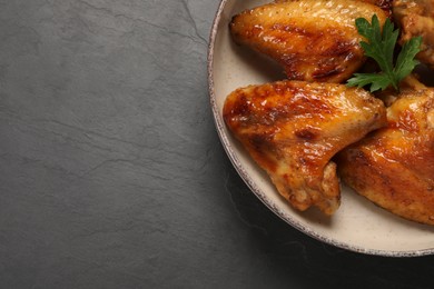 Photo of Bowl with delicious fried chicken wings on black table, top view. Space for text