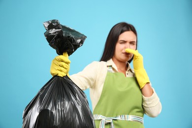 Photo of Woman holding full garbage bag against light blue background, focus on hand