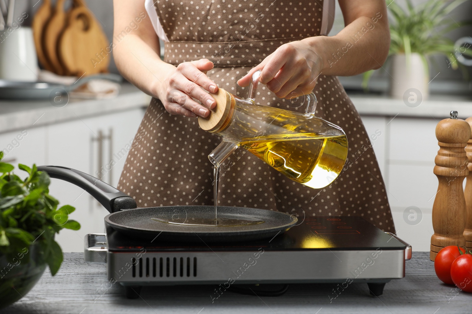 Photo of Vegetable fats. Woman pouring cooking oil into frying pan on stove in kitchen, closeup