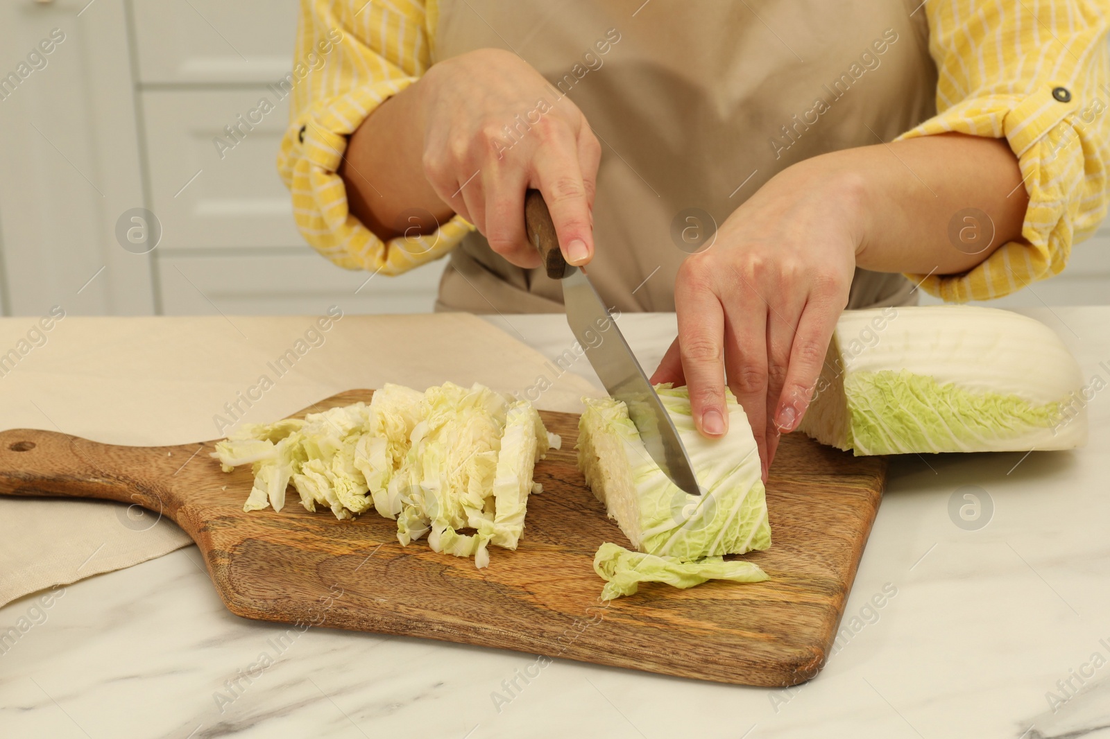 Photo of Woman cutting fresh chinese cabbage at table in kitchen, closeup