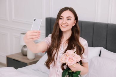 Beautiful young woman taking selfie with rose flowers on bed in room