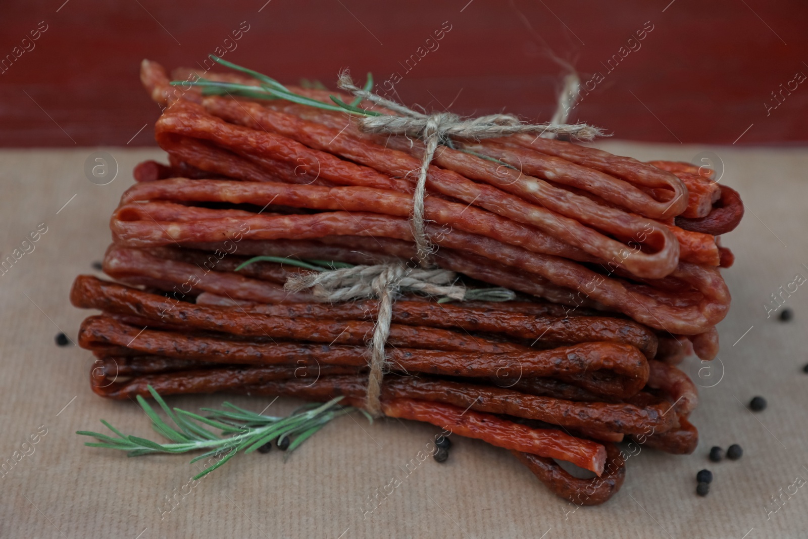 Photo of Tasty dry cured sausages (kabanosy) and spices on parchment paper, closeup