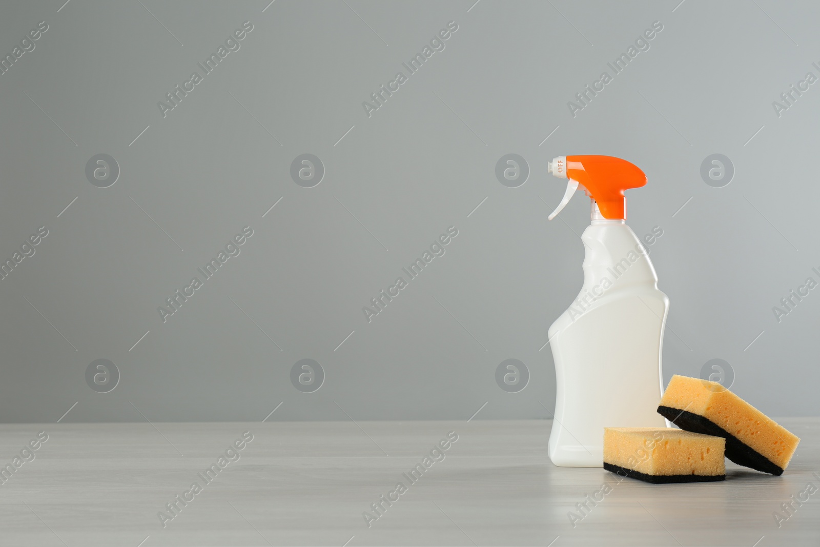 Photo of Bottle of cleaning product and sponges on light table. Space for text