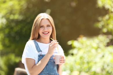 Photo of Young woman with cup of delicious milk shake outdoors