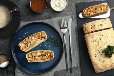 Photo of Pieces of delicious strudel with chicken and vegetables served on grey textured table, flat lay