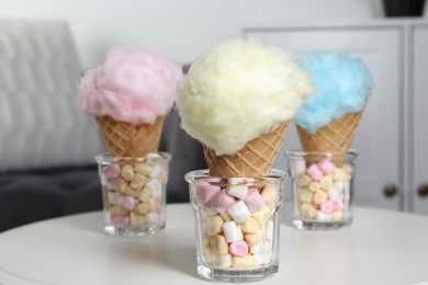 Photo of Sweet cotton candies in waffle cones and marshmallows on white table indoors, closeup