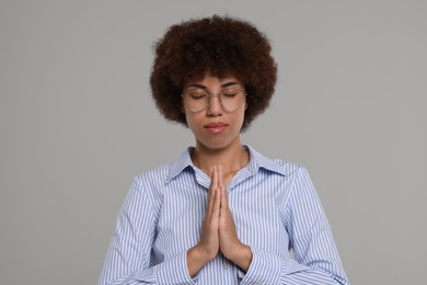 Woman with clasped hands praying to God on grey background